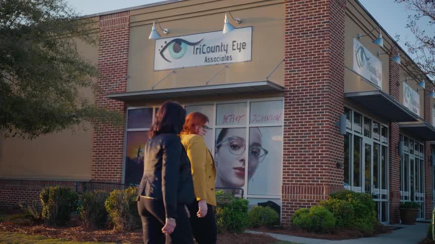A trio of women walk together outside of a shop that sells eyeglasses