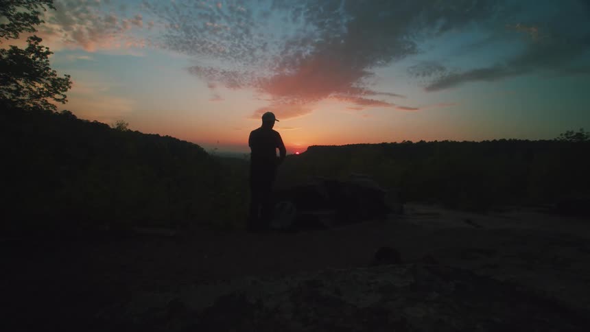 Silhouette of two men in a natural environment with mountains around and sunrise on the horizon