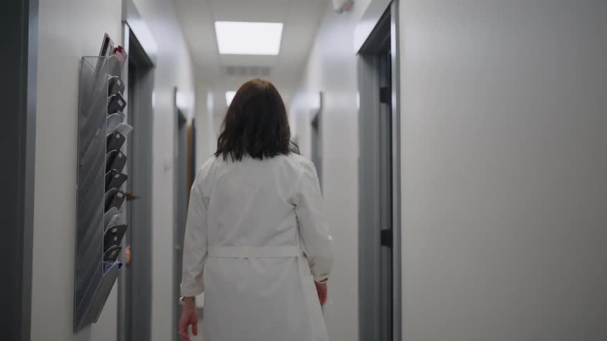 A woman in white clothing is walking down a hallway and entering a room