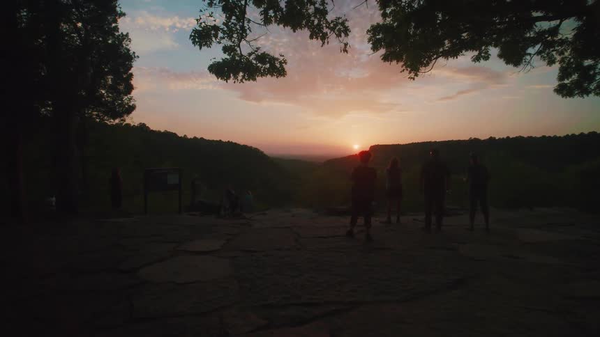 Four people stand on stones at the edge of a summit at sunrise