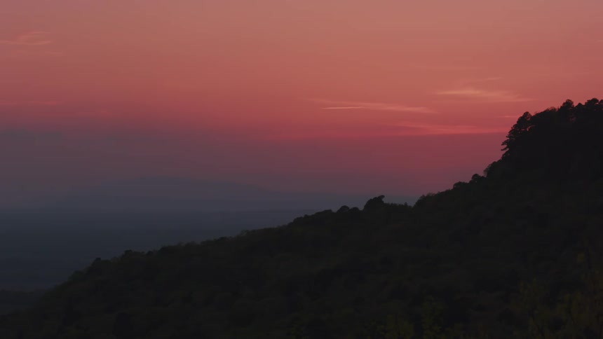 A sunset with a gradient of pink and orange hues over a silhouette of a mountain