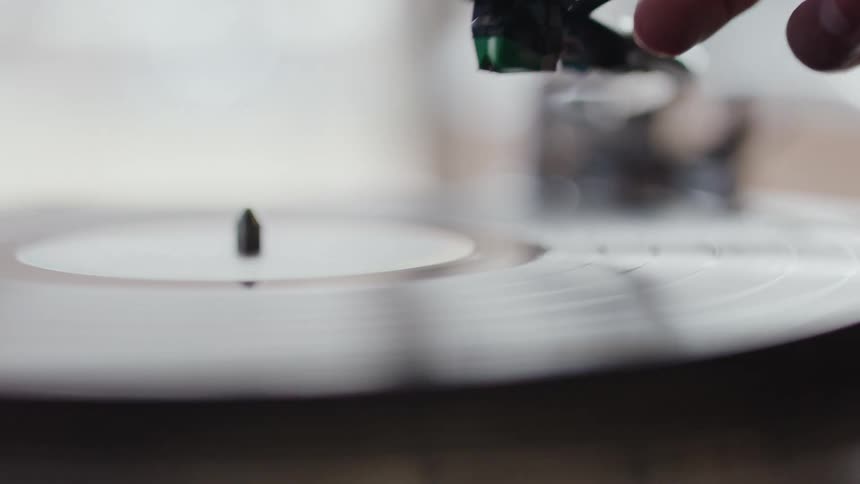 Vinyl record playing and a persons hand removing the instrument