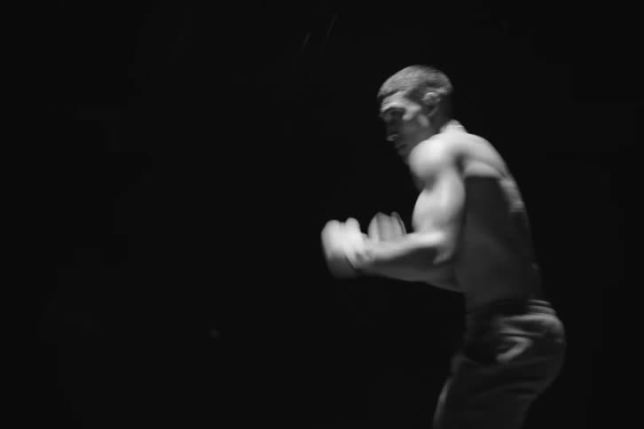 A shirtless male boxer is boxing in the rain at night captured in black and white