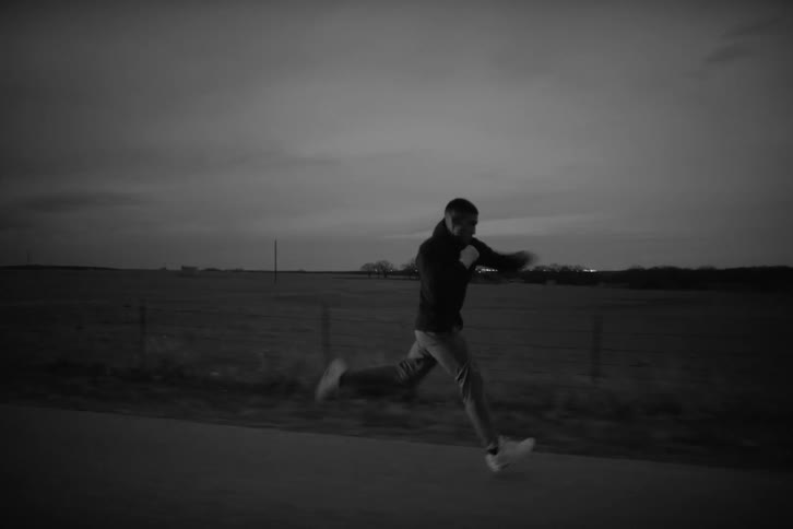 Man running on the road next to a field and doing boxing punches