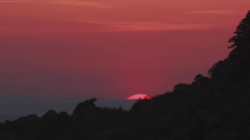 The sun is setting beyond the trees on the mountain and the water