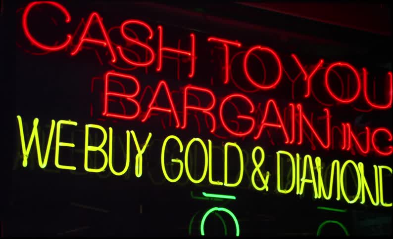 Person walks past glowing sign for a gold and diamond buying store