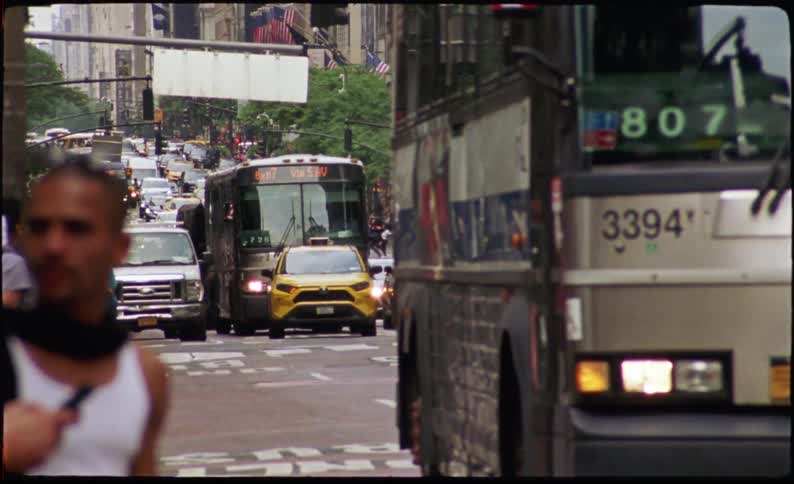 A busy urban street scene with multiple vehicles including buses and yellow cabs