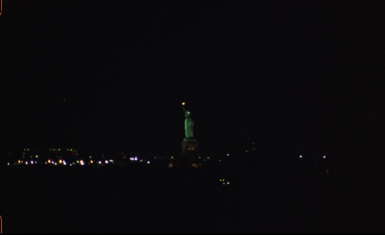 The statue of liberty is illuminated in the dark of night as a boat passes by