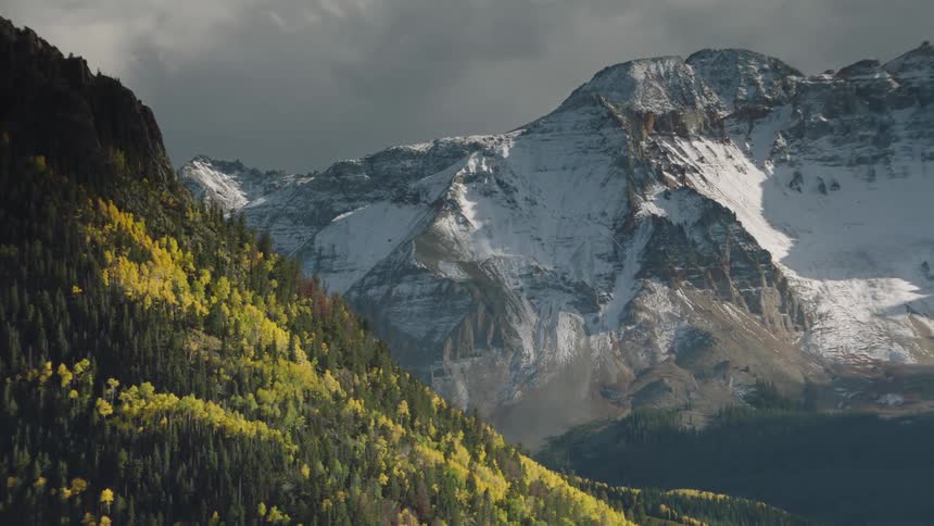 A huge stone mountain covered in snow and on the left side there is a mountain with forest and covered with vegetation