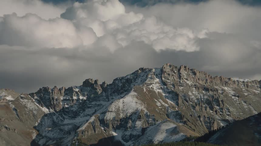 Conifer forest leads to snowy mountains under heavy dark clouds