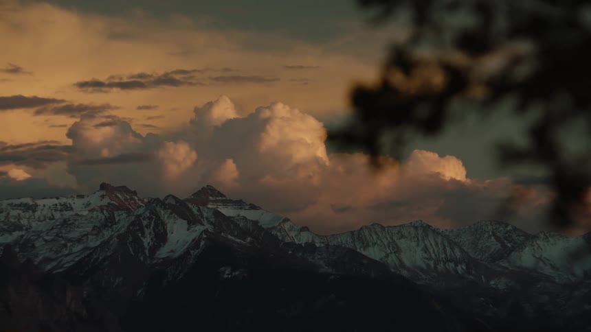 Large clouds sit on snowcapped mountains at dusk