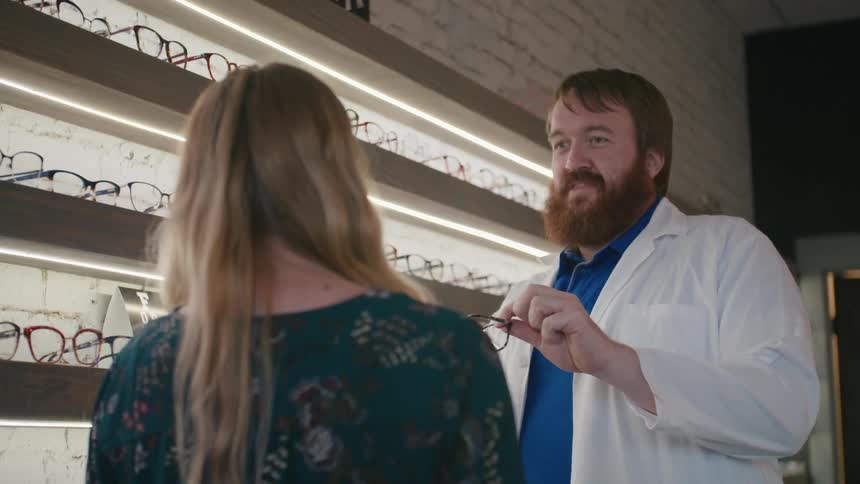 Man in a lab coat handing prescription glasses to a female patient