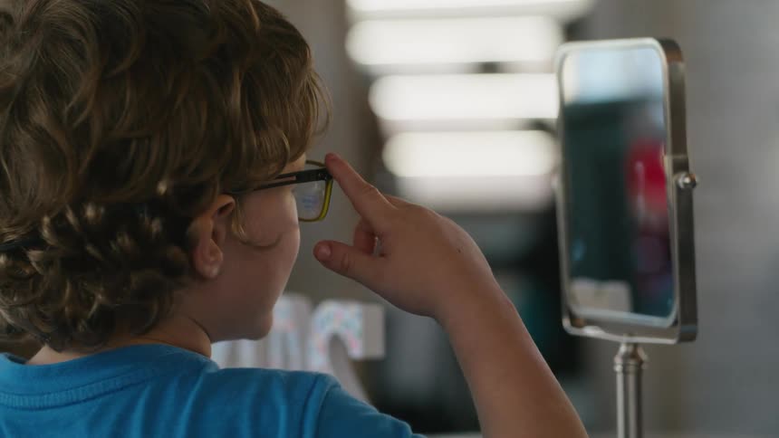 A child with curly hair trying new glasses in front of a mirror
