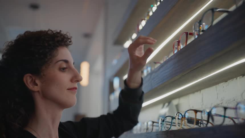 A woman organizing a shelf of eyeglasses in a store