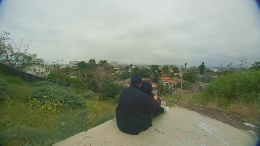 View of a couple with their backs hugging and sitting on a rock overlooking an urban city