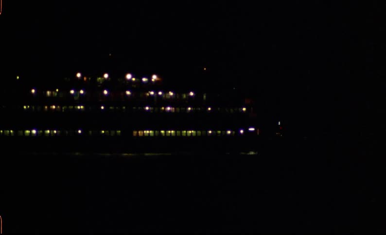 A large ship with many lights travels steadily across the water at night