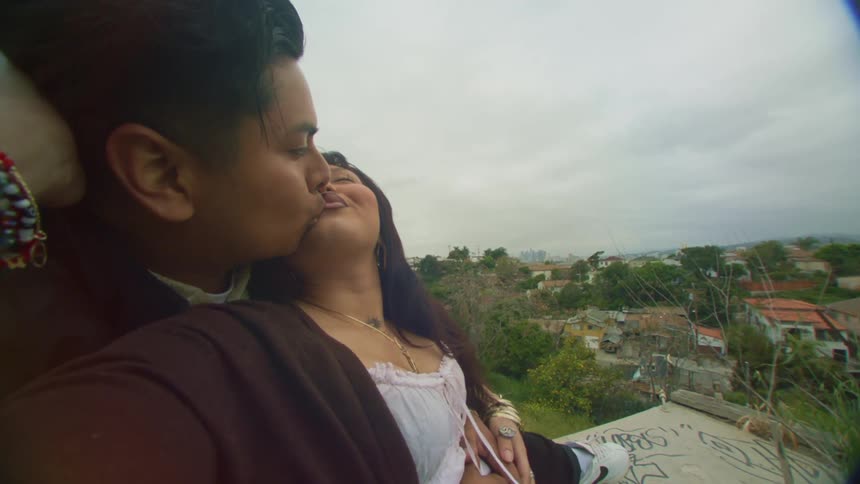 A young happy couple kissing on a hill next to town