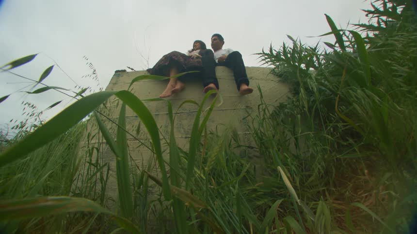 A barefoot couple sitting atop a concrete wall in the countryside
