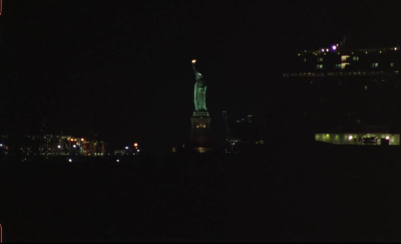 A large cruise ship crosses in front of a lighted statue at the edge of a metropolis