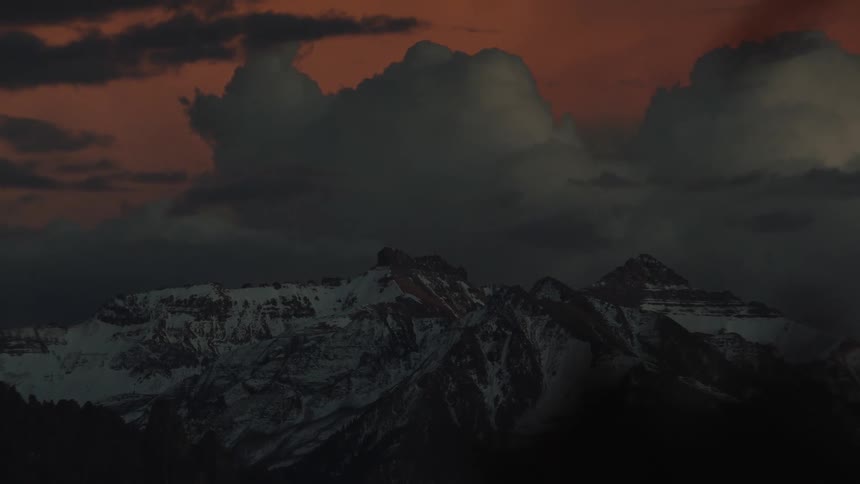 Mountains and cliffs with snow and a reddish and cloudy sky at dawn