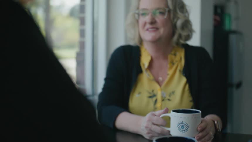 Two friends sitting next to a window enjoy a cup of coffee