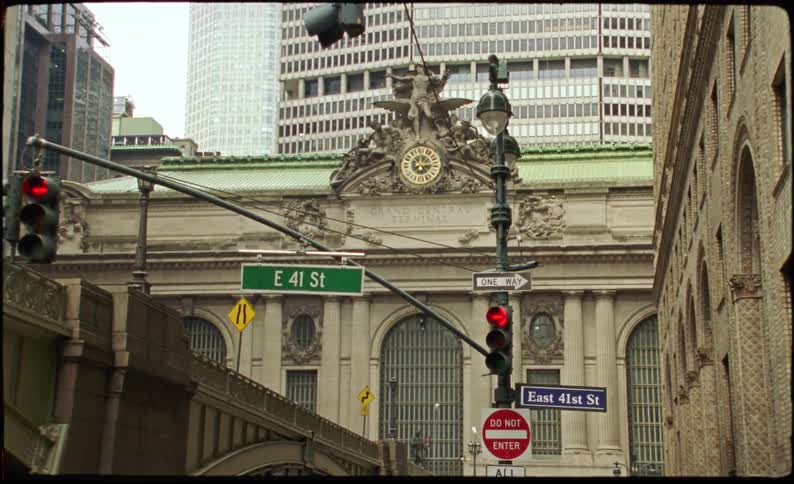 Street of a metropolis with vehicle traffic and a historic building with the monument of an angel above a clock