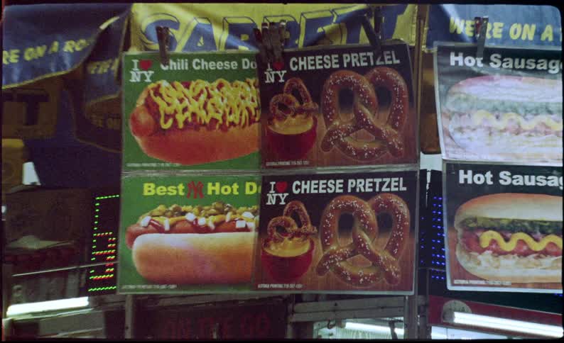 Several hanging signs advertising food and a neon sign next to it