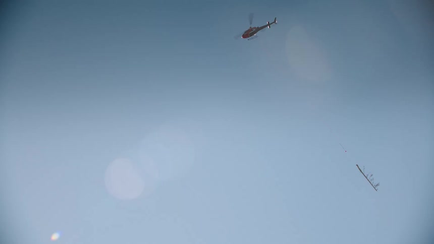 A helicopter carries a long tree trunk across the clear blue sky