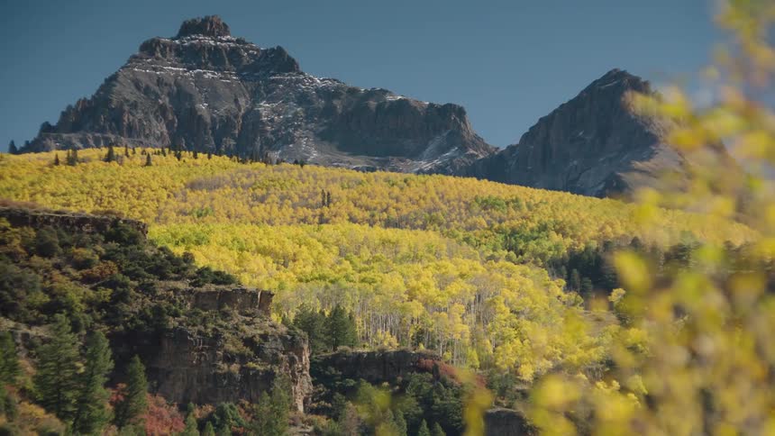Natural landscape of hills with forest of yellow trees and peaks with cliffs against a cloudless blue sky