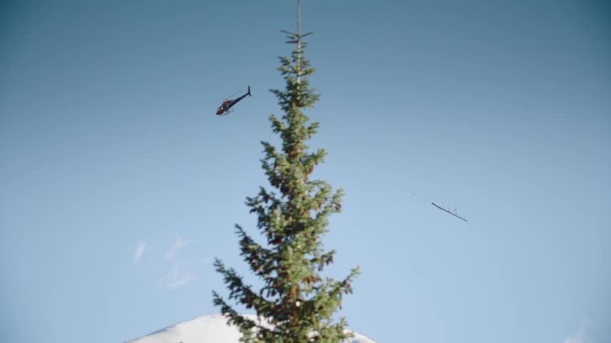 A helicopter carrying a log over the mountains