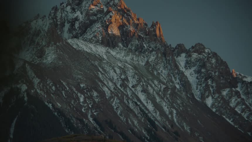 A rugged mountain peak with snow and the last light of sunset hitting its peak