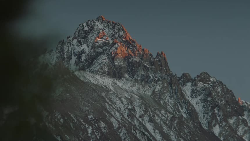A rugged mountain peak with snow and the last light of sunset hitting its peak