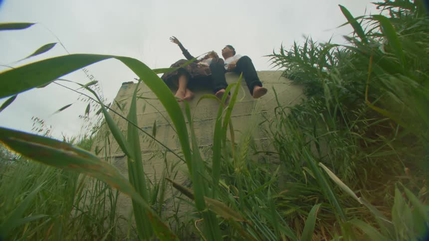 A barefoot couple sitting on a concrete wall over a grassy field