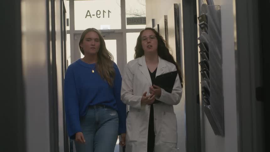 A doctor and a patient walk down a narrow corridor
