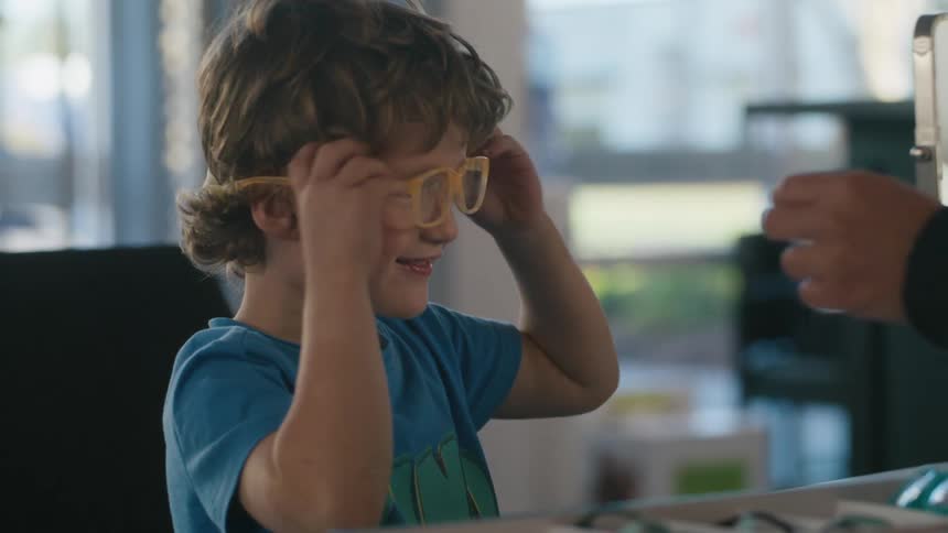 Little boy trying on yellow prescription glasses smiling