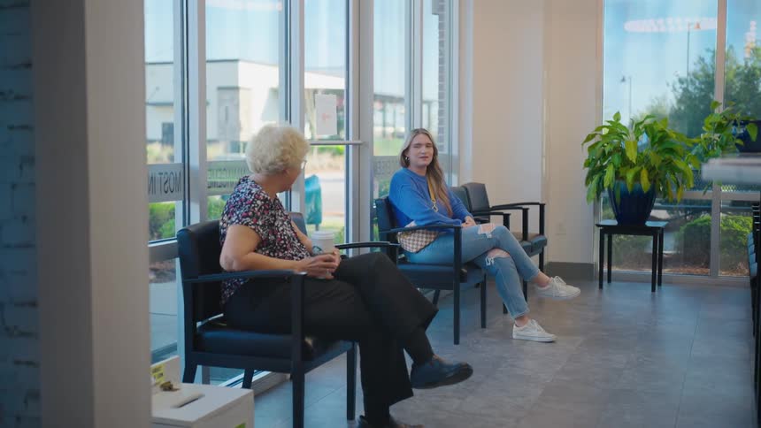 Young woman and an elderly woman sitting at the reception of a clinic talking