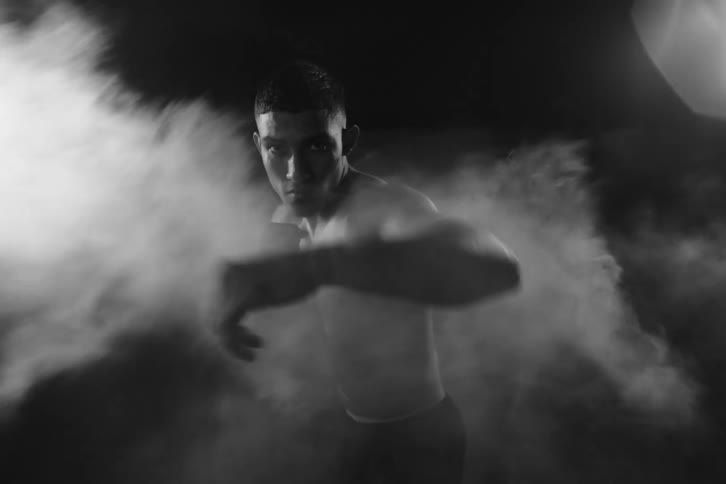 A man is not throwing rapid punches forward in black and white tones as white smoke passes over him