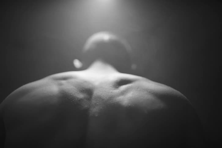 Back of a muscular shirtless man under a spotlight at night