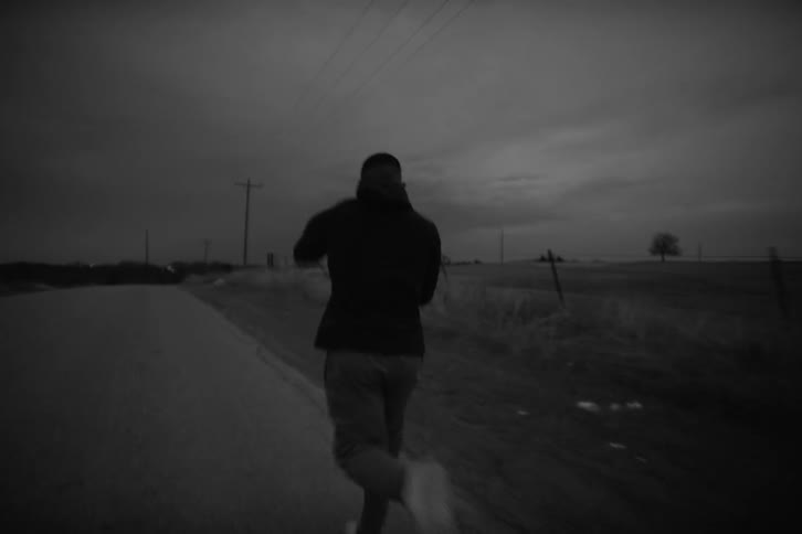 Man in sweatshirt and pants running on an isolated road next to fields and throwing boxing punches in the air