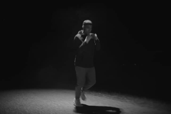 A boxer in a hoodie and pants is practices while jogging on a road at night