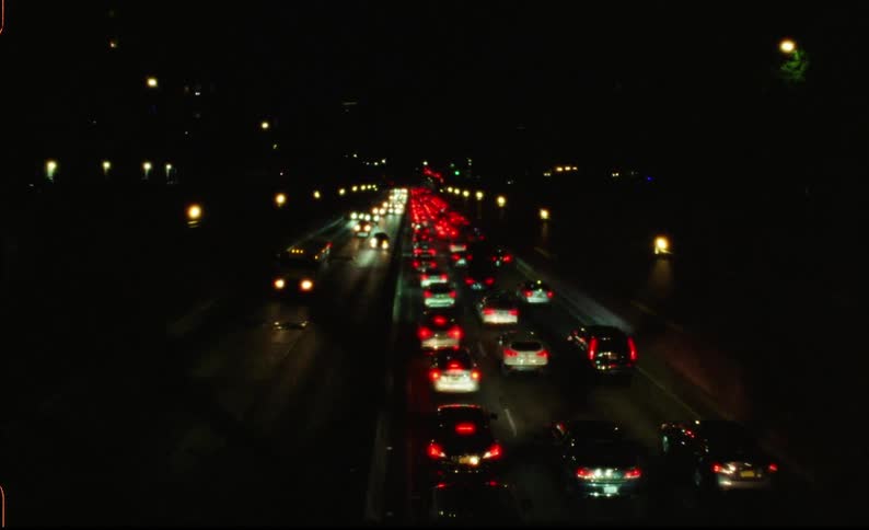 Nighttime traffic with rows of cars with tail lights illuminating a dark road