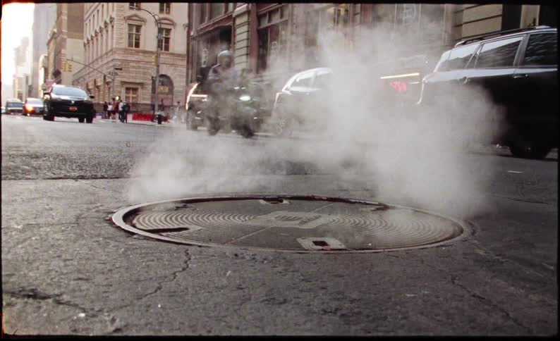 A manhole cover on an urban street with steam rising from it