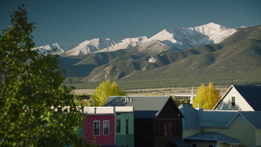 Residential neighborhood sits across paved area from green and snowy mountains