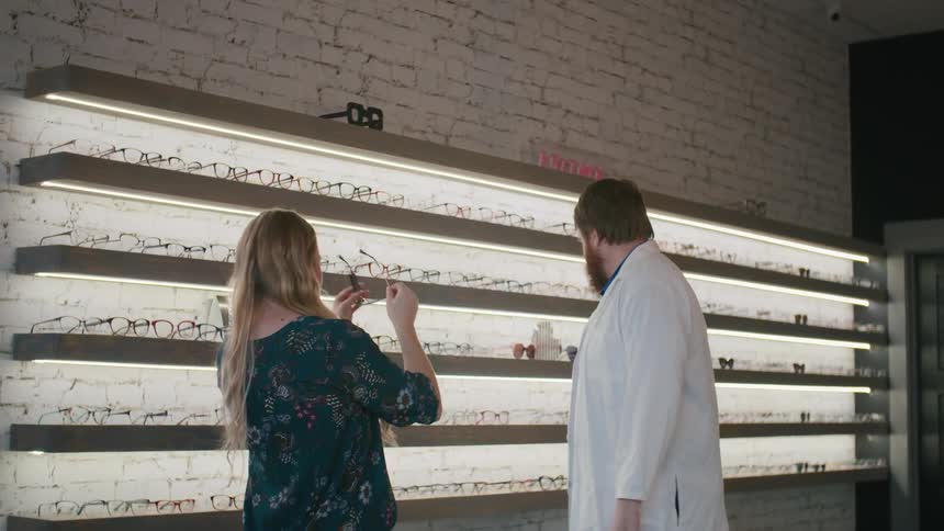 An optician offers a female customer a pair of glasses to try on