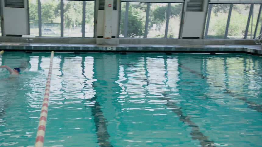 Man jumps into indoor swimming pool while others swim laps