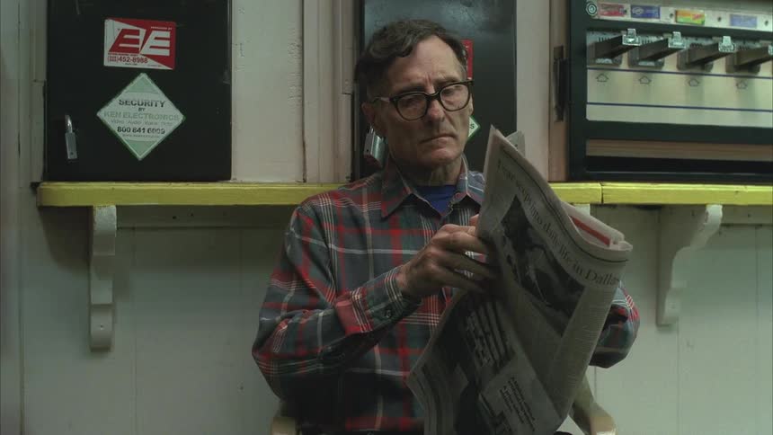 An older man is sitting and reading a newspaper inside a laundromat