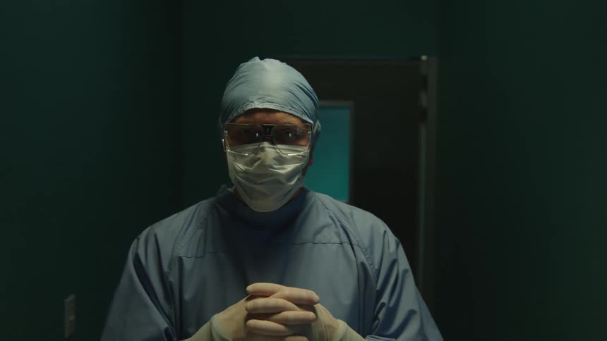 Surgeon doctor with glasses clothes and protective mask entering inside a dark room in hospital