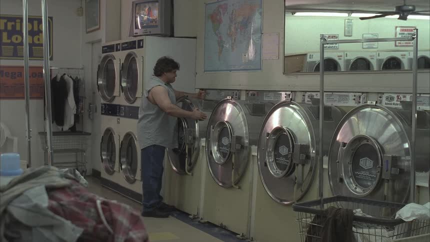 An impatient man kicks and punches a washing machine in a laundromat