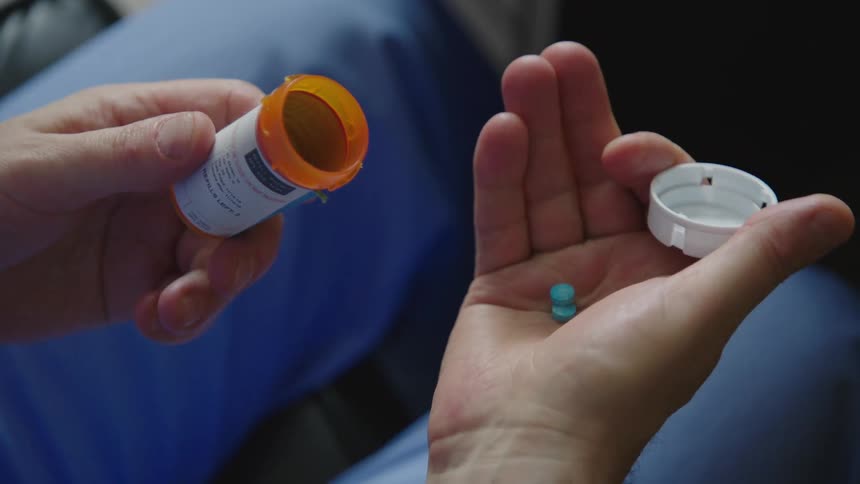 A doctor having a nervous breakdown opens a pill bottle and takes two pills