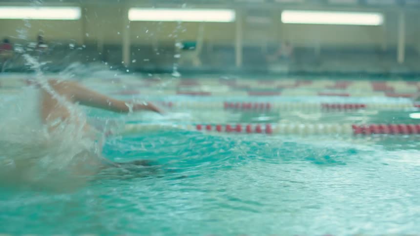 Man swims quickly while exercising in lane in large swimming pool